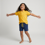 Kid wearing Kiggle Classic Polo in Mustard with navy terry shorts