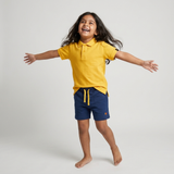 Kid wearing Kiggle Classic Polo in Mustard with navy terry shorts