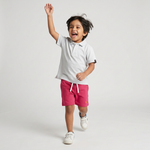 Kid wearing Kiggle Classic Polo in Snow with raspberry terry shorts